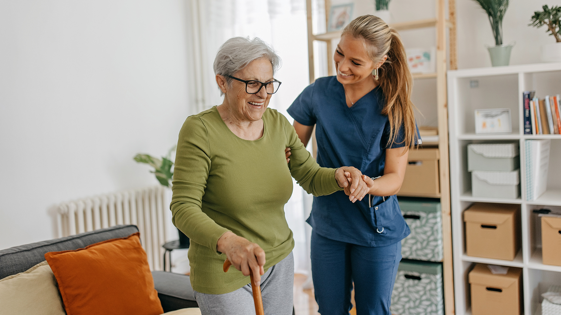 senior woman walking with a cane with the help of her caregiver in lifecare