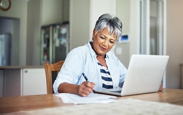 senior woman sitting at a table with her laptop and financial documents in front of her